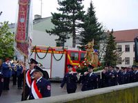 Die Feuerwehr zieht mit der Statue des hl. Florian auf den Schultern vor dem geschm&uuml;ckten LF 16 auf dem Kirchplatz vorbei