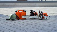 zwei Motors&auml;gen mit Kraftstoffkanister und Helm mit Forstvisier auf dem Boden